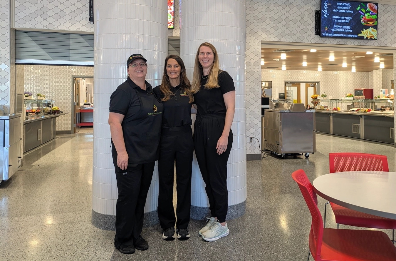 Three Waltham school nutrition leaders standing inside a school cafeteria